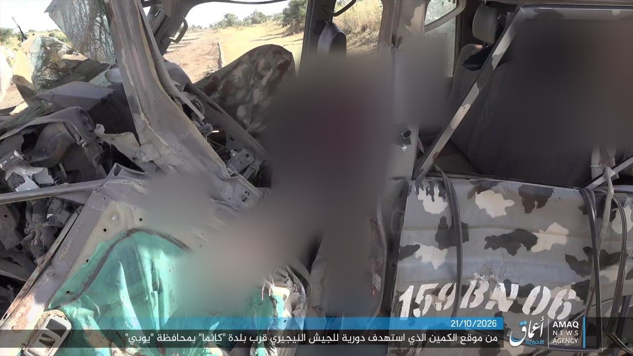 Destroyed Nigerian army pickup truck with camouflage paint and the stenciled marking 159BN06 on its side; the cab area is heavily blurred; an Amaq News Agency caption bar dated 21/10/2026 runs along the bottom.