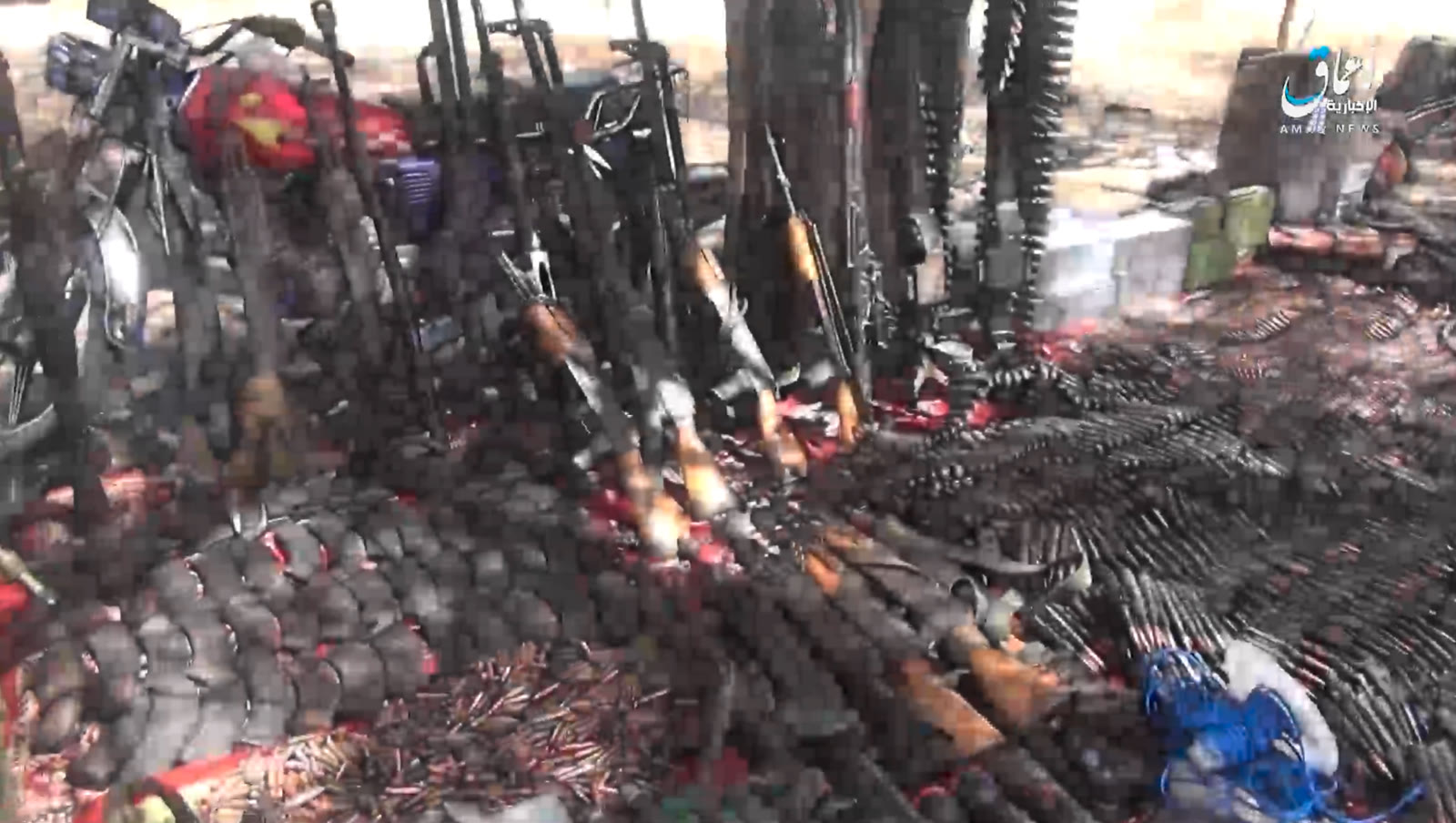 Captured weapons display Daytime overhead view of captured rifles, machine guns, and belts of ammunition laid out on a patterned rug, with an Amaq News Agency watermark in the top-right corner