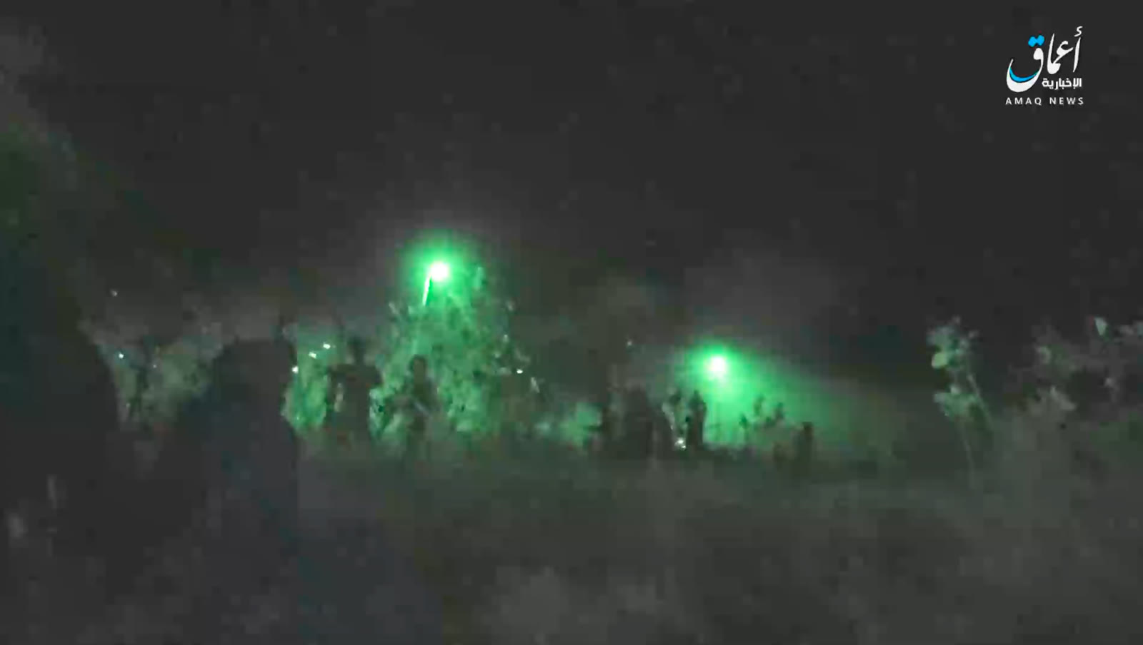 Night-vision assault frame Green night-vision frame showing several standing figures and bright flares across open ground, with an Amaq News Agency watermark in the top-right corner