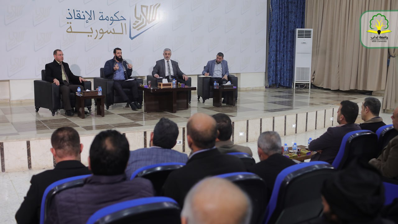 Al-Julani seated on a stage with three other men before an audience in blue tiered seats, December 6, 2023.