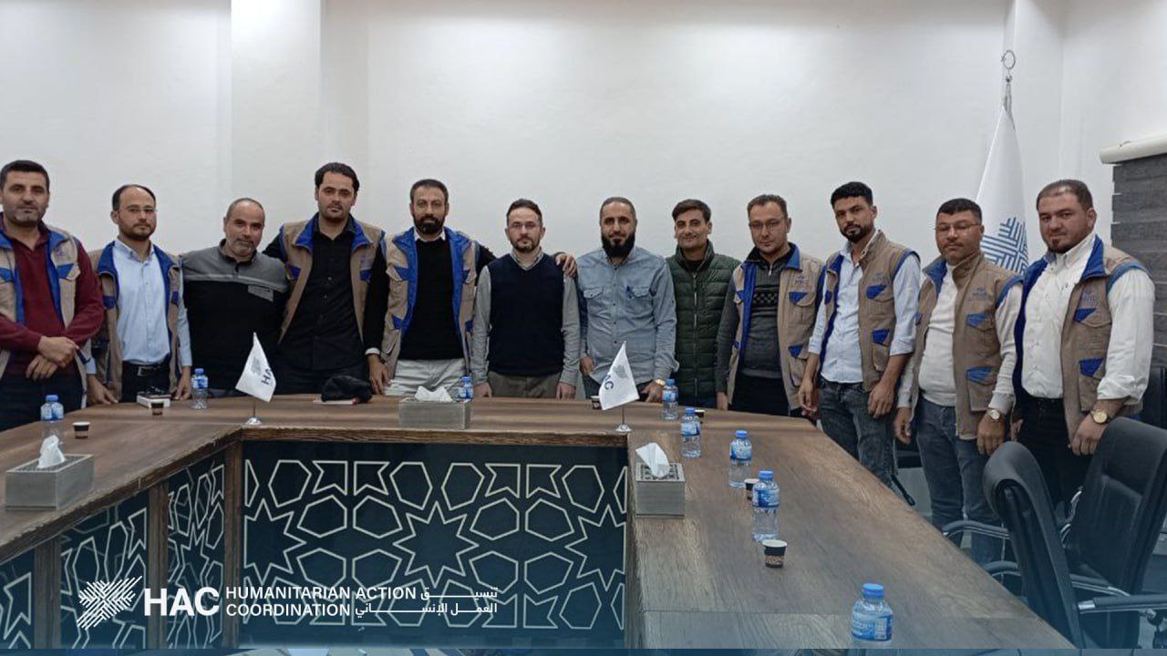 Workshop group photo at a humanitarian office with a patterned table covering, November 17, 2023.