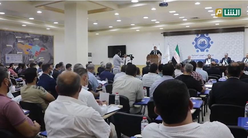 A Syria TV photo of a large Bab al-Hawa hall with round tables, a ceiling projector, and a lectern.