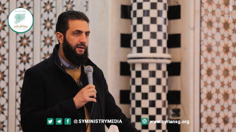 Al-Julani speaking into a microphone in front of a black-and-white checkered column and lattice wall inside a mosque, March 10, 2024.