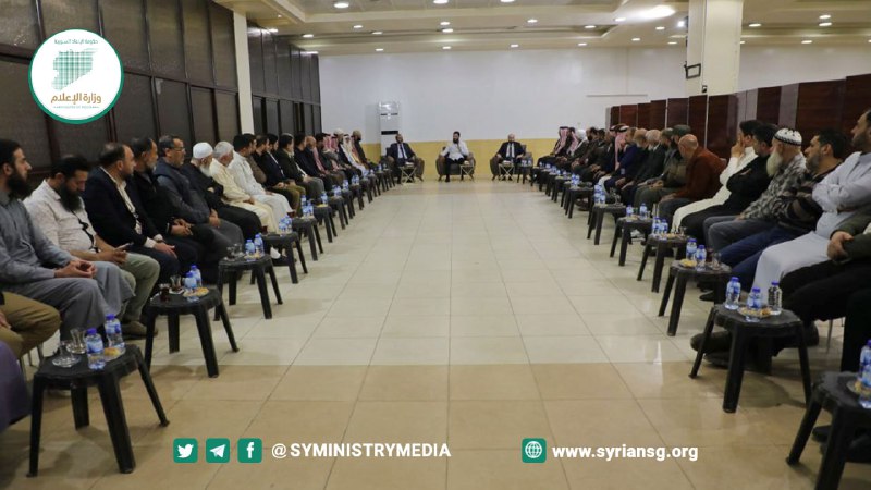 Displaced notables seated in long rows along both walls of a hall, with al-Julani at the far end, April 12, 2024.