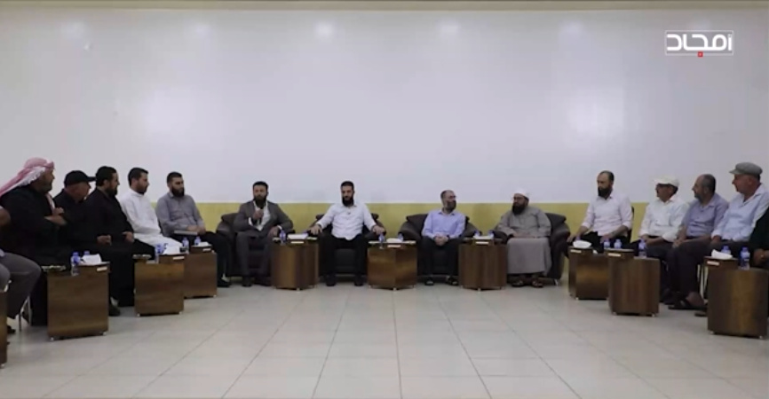 The September 2023 meeting in the same hall, men seated along the walls.