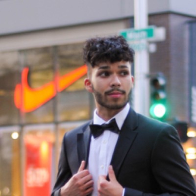 LinkedIn profile photo of Salim Ghulam Nabi in a black tuxedo and bow tie, standing on a city sidewalk in front of a Nike store.